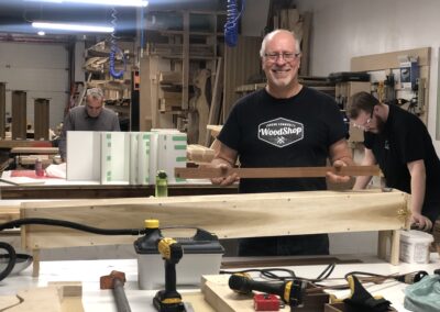 Andrew with a busy workstation in the woodshop with other woodworkers in the background, tools in the foreground