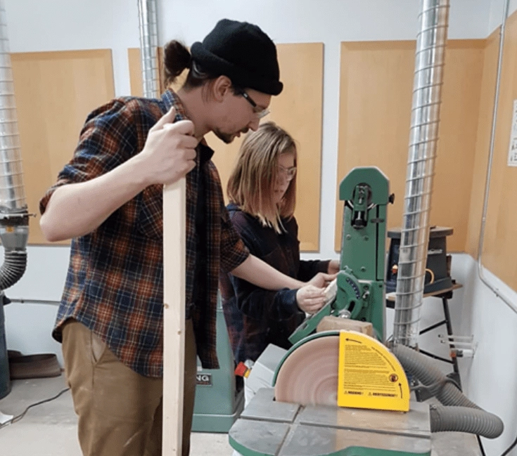 Devon Curtis teaching a student at a saw in the woodshop